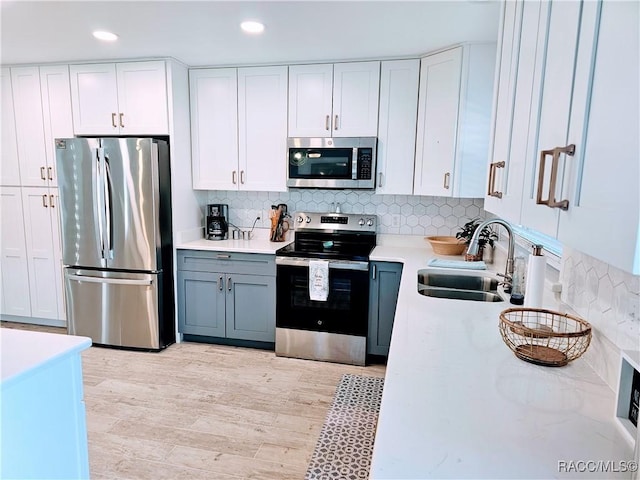 kitchen featuring white cabinets, appliances with stainless steel finishes, light countertops, light wood-type flooring, and a sink