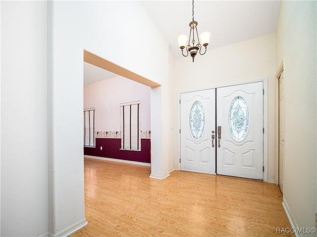 entryway with a towering ceiling, a chandelier, and light wood-type flooring