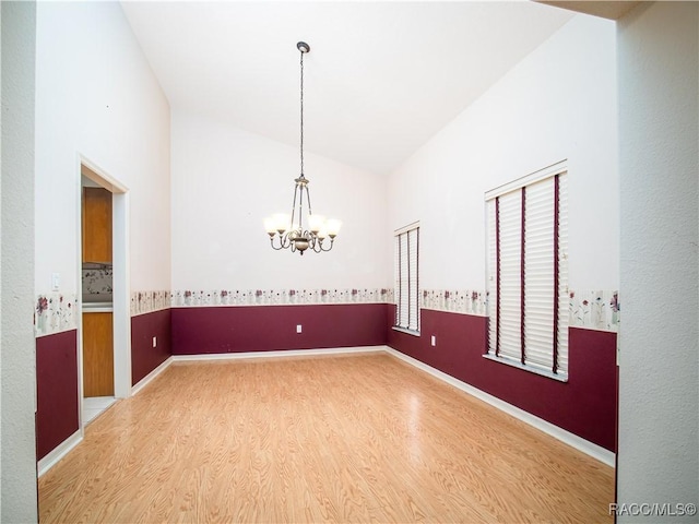 empty room with hardwood / wood-style flooring, a chandelier, and vaulted ceiling