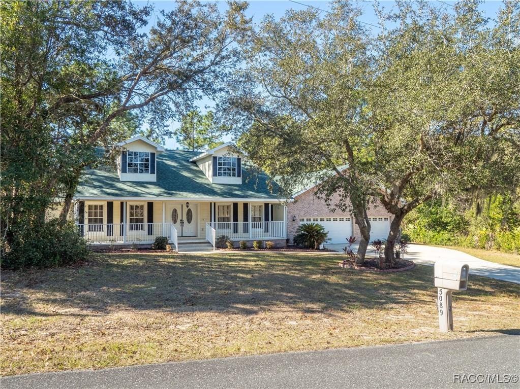 cape cod-style house with a garage, covered porch, and a front yard