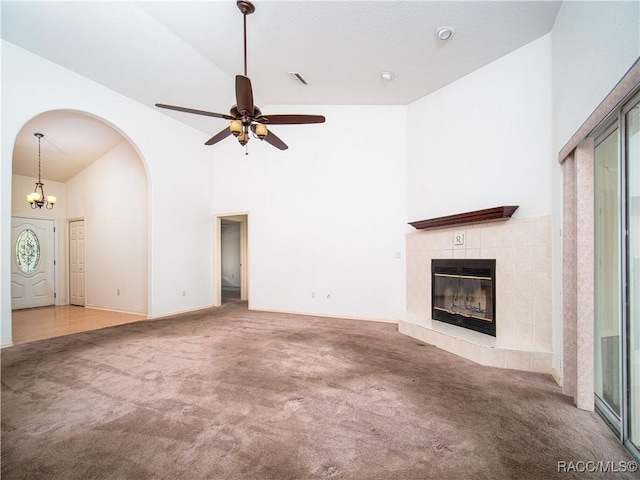 unfurnished living room with a tiled fireplace, carpet floors, ceiling fan with notable chandelier, and high vaulted ceiling