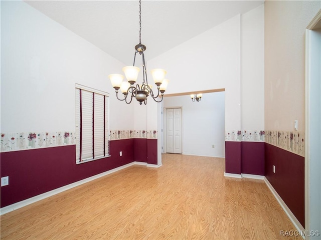 empty room with a notable chandelier, vaulted ceiling, and hardwood / wood-style floors