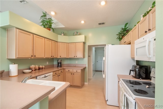 kitchen with white appliances, a textured ceiling, light brown cabinetry, and light hardwood / wood-style flooring