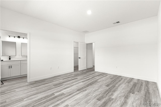 unfurnished bedroom with light wood-style floors, visible vents, baseboards, and ensuite bathroom