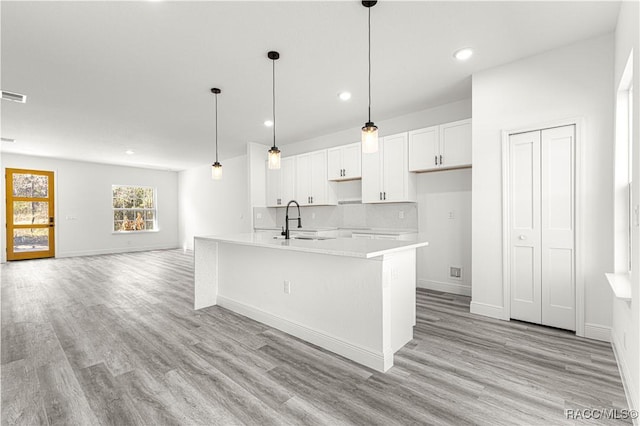 kitchen featuring pendant lighting, a center island with sink, light countertops, decorative backsplash, and white cabinetry