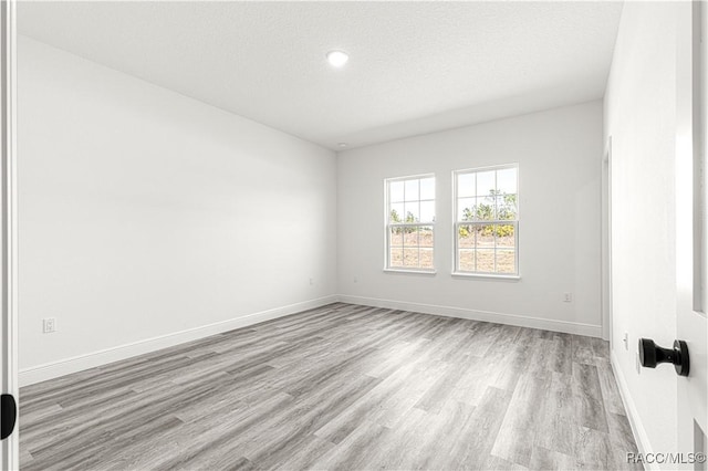 empty room with light wood-style floors, a textured ceiling, and baseboards