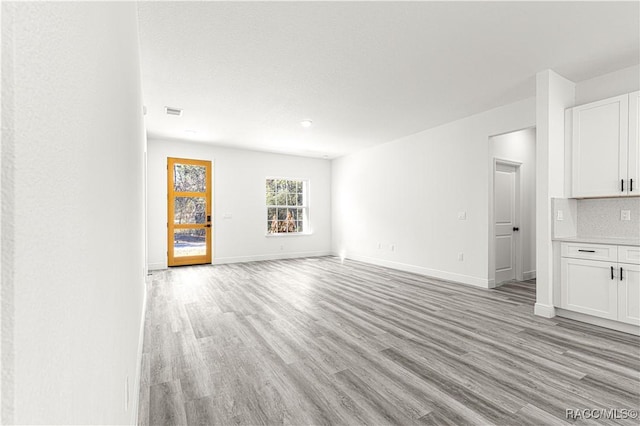 unfurnished living room with light wood-type flooring, visible vents, and baseboards