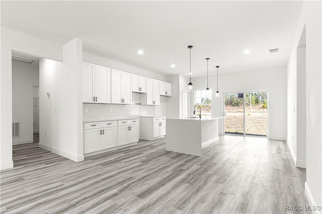 kitchen with white cabinets, light countertops, hanging light fixtures, and an island with sink