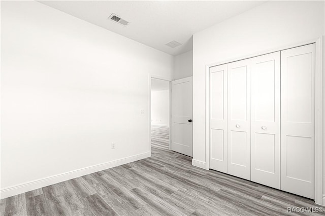 unfurnished bedroom featuring baseboards, a closet, visible vents, and light wood-style floors