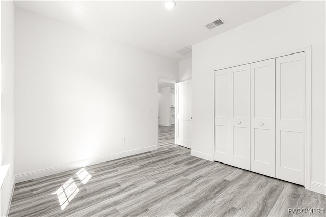 unfurnished bedroom with a closet, baseboards, visible vents, and light wood finished floors