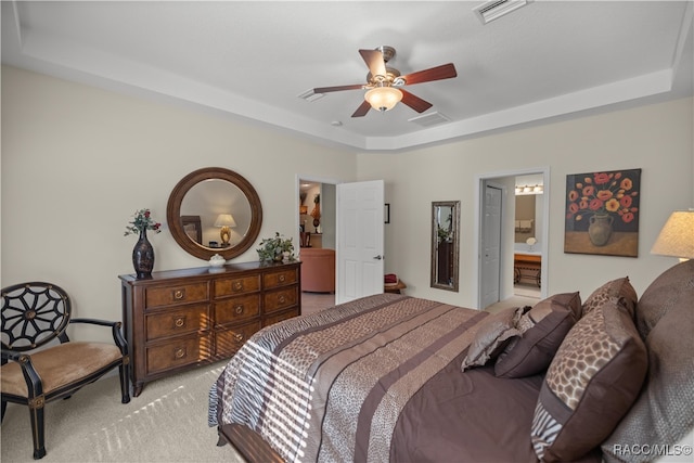 carpeted bedroom featuring a tray ceiling, ensuite bathroom, and ceiling fan