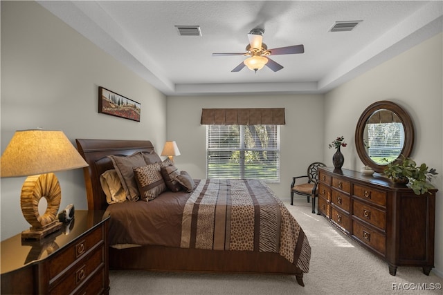 carpeted bedroom with a textured ceiling, a raised ceiling, and ceiling fan