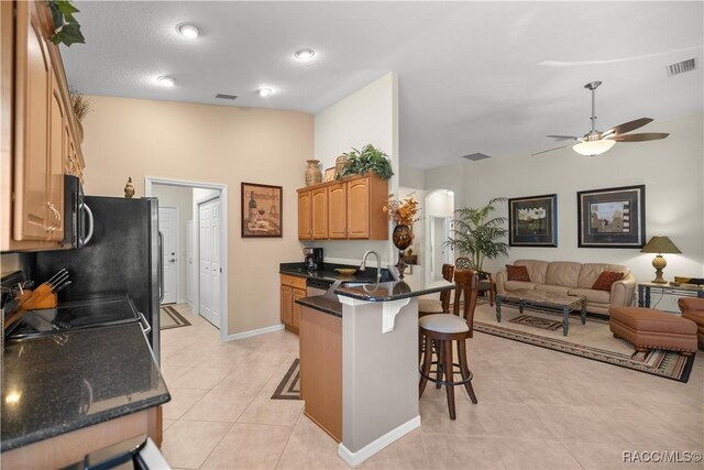 kitchen with a kitchen bar, kitchen peninsula, ceiling fan, and dark stone countertops