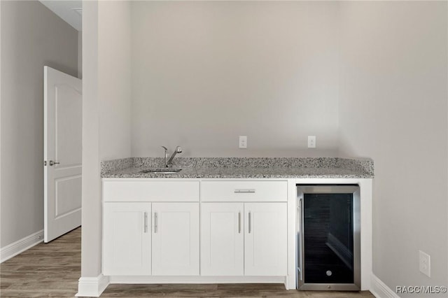 bar featuring white cabinets, sink, hardwood / wood-style flooring, light stone counters, and beverage cooler