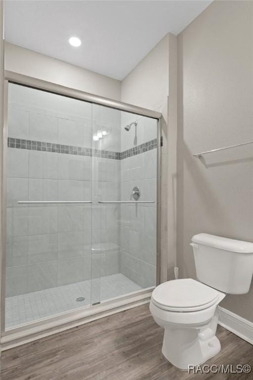 bathroom with hardwood / wood-style floors, a shower with door, and toilet