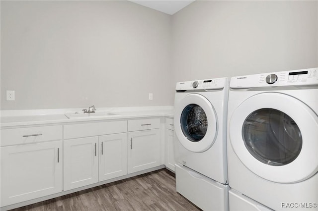 washroom featuring washing machine and clothes dryer, cabinets, sink, and hardwood / wood-style floors