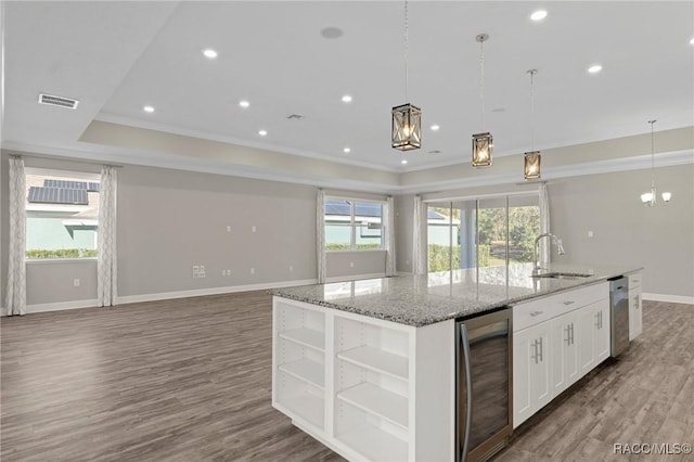 kitchen featuring beverage cooler, sink, decorative light fixtures, white cabinets, and an island with sink