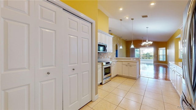 kitchen with light tile patterned flooring, kitchen peninsula, stainless steel appliances, and hanging light fixtures