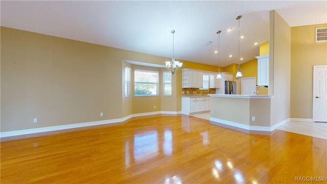 unfurnished living room featuring light wood-type flooring, vaulted ceiling, and a chandelier