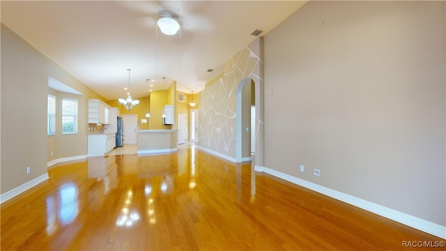 unfurnished living room featuring light hardwood / wood-style floors, a notable chandelier, and vaulted ceiling