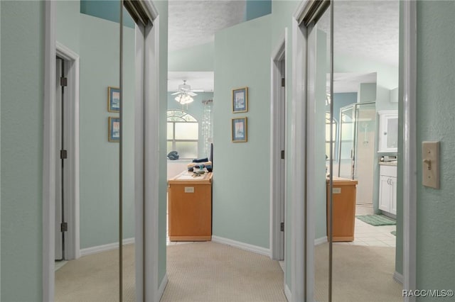 corridor featuring light colored carpet, baseboards, and a textured ceiling