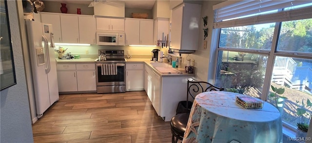 kitchen featuring white appliances, wood finished floors, a sink, light countertops, and white cabinets