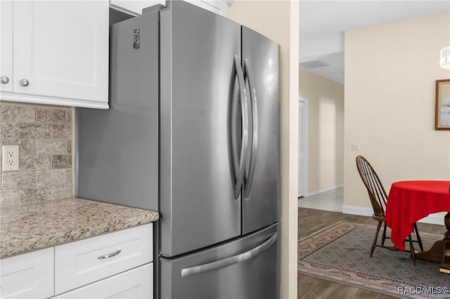 kitchen featuring dark wood-type flooring, stainless steel fridge, light stone countertops, white cabinets, and decorative backsplash