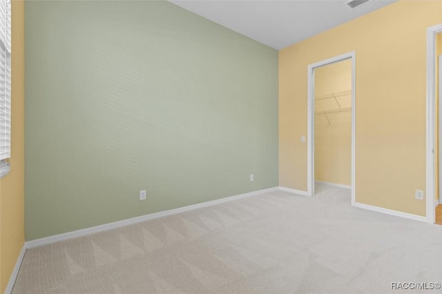 unfurnished bedroom with light colored carpet, a walk in closet, and a closet