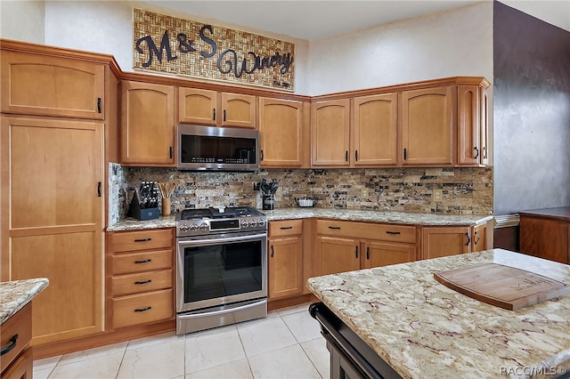 kitchen featuring light tile patterned floors, stainless steel appliances, light stone counters, and tasteful backsplash