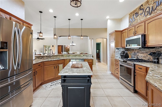 kitchen with light stone countertops, stainless steel appliances, ceiling fan, sink, and hanging light fixtures