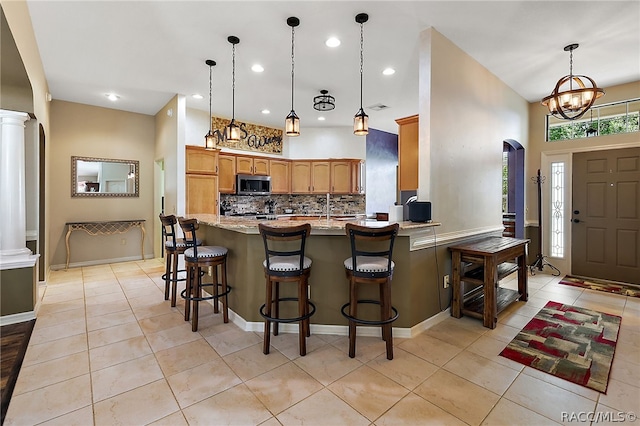 kitchen with light stone countertops, tasteful backsplash, decorative light fixtures, a kitchen bar, and light tile patterned flooring