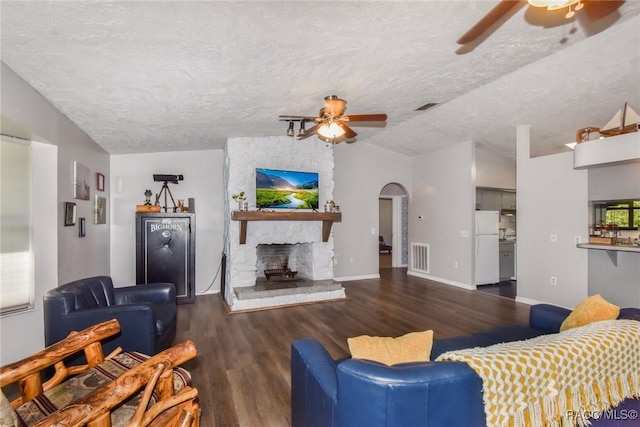 living room with vaulted ceiling, a stone fireplace, ceiling fan, dark wood-type flooring, and a textured ceiling