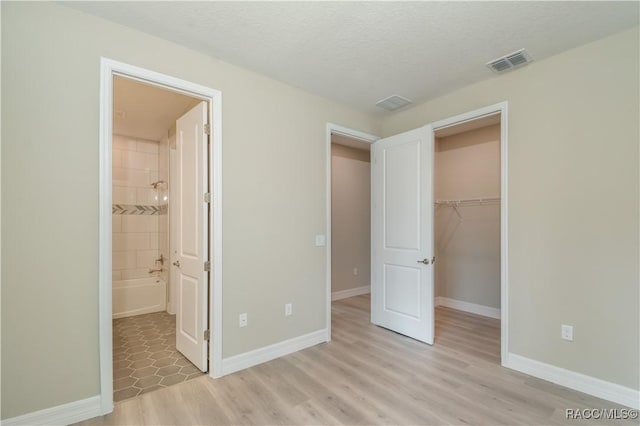 unfurnished bedroom with a closet, ensuite bath, a textured ceiling, a walk in closet, and light wood-type flooring