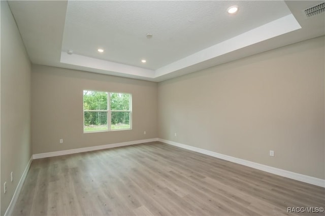 spare room featuring light wood-type flooring, a textured ceiling, and a raised ceiling