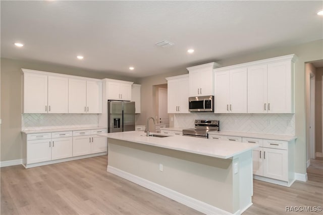 kitchen with appliances with stainless steel finishes, sink, light wood-type flooring, white cabinets, and an island with sink