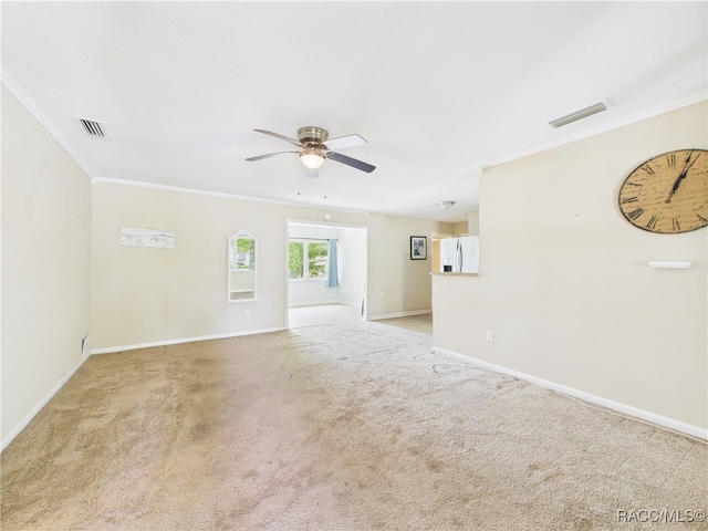 spare room with a ceiling fan, crown molding, light colored carpet, and baseboards