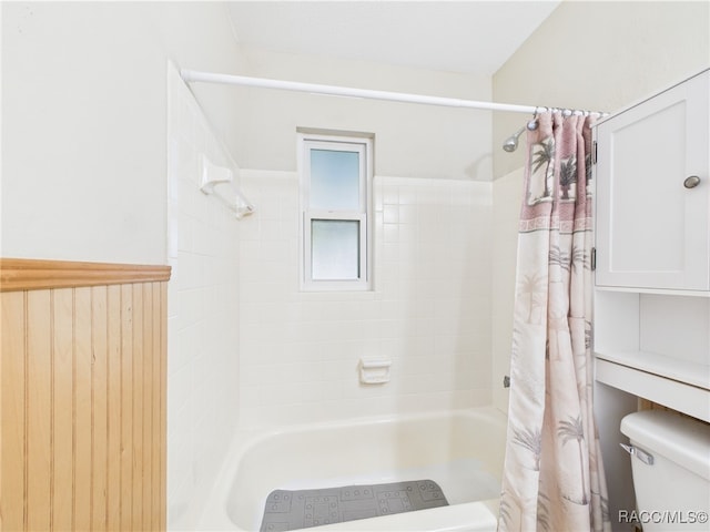 full bathroom with toilet, shower / tub combo with curtain, and a wainscoted wall