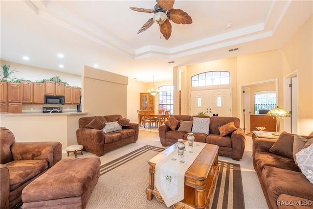 carpeted living room featuring ceiling fan with notable chandelier, plenty of natural light, and a raised ceiling