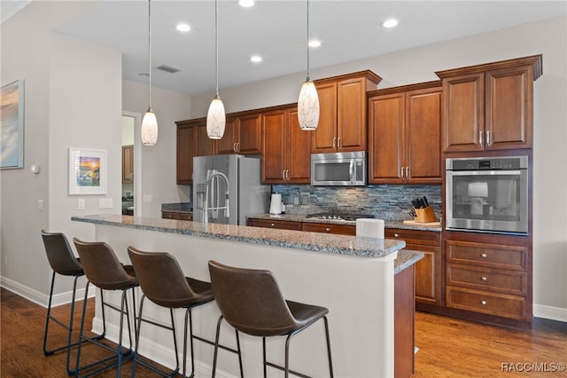 kitchen with hardwood / wood-style floors, a breakfast bar, dark stone countertops, an island with sink, and stainless steel appliances