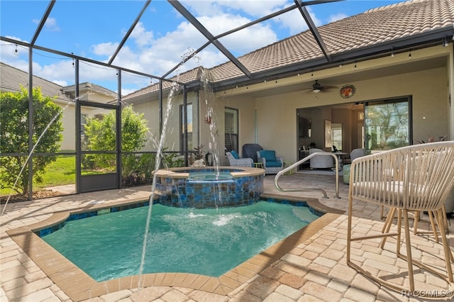 view of pool featuring glass enclosure, pool water feature, ceiling fan, an in ground hot tub, and a patio area