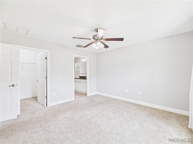 1899 W Oliver Dr, Citrus Springs, FL 34434 - unfurnished bedroom featuring light carpet, a walk in closet, a closet, a ceiling fan, and connected bathroom