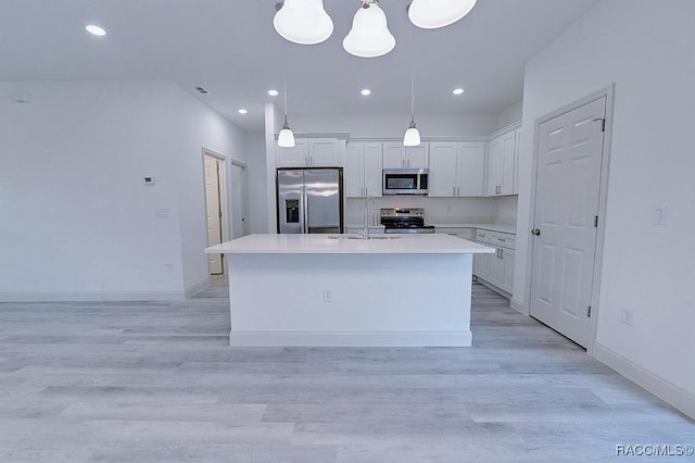 kitchen featuring appliances with stainless steel finishes, light wood-type flooring, a kitchen island with sink, pendant lighting, and white cabinetry