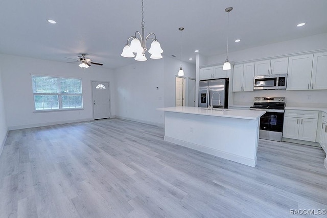 kitchen featuring appliances with stainless steel finishes, ceiling fan with notable chandelier, a kitchen island with sink, white cabinetry, and hanging light fixtures