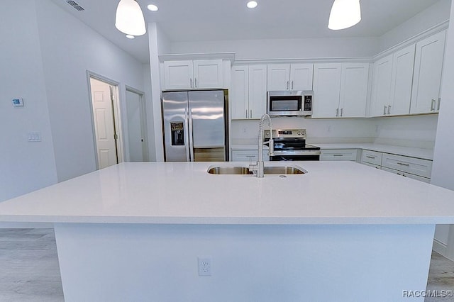 kitchen with appliances with stainless steel finishes, white cabinetry, a kitchen island with sink, and sink