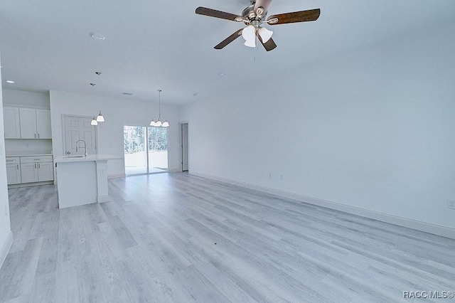 unfurnished living room with ceiling fan with notable chandelier, light hardwood / wood-style floors, and sink