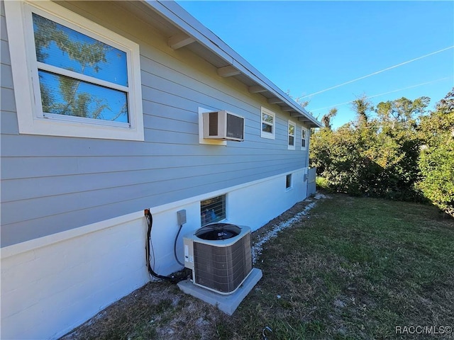 view of side of home with a wall unit AC, central AC unit, and a lawn