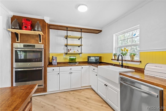 kitchen with sink, appliances with stainless steel finishes, butcher block counters, white cabinetry, and ornamental molding