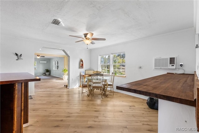 unfurnished dining area with a textured ceiling, light hardwood / wood-style floors, a wall mounted AC, and ceiling fan