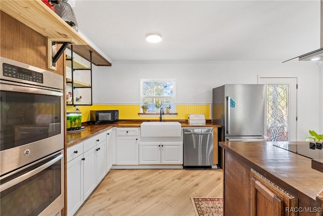 kitchen featuring sink, white cabinetry, wooden counters, light hardwood / wood-style flooring, and black appliances