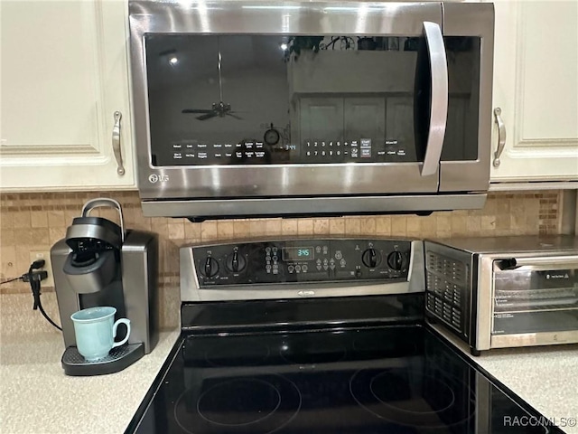 room details featuring appliances with stainless steel finishes, decorative backsplash, white cabinetry, and ceiling fan